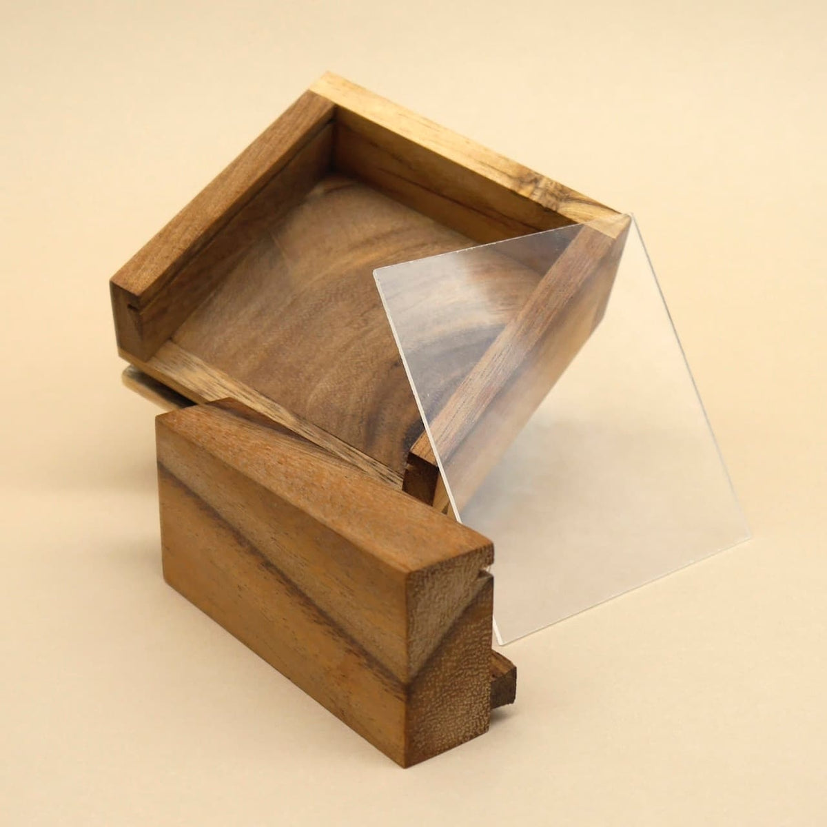 Zerlegtes Geduldspiel aus Holz mit teilweise herausgezogener Acrylscheibe, Einzelteile locker arrangiert.