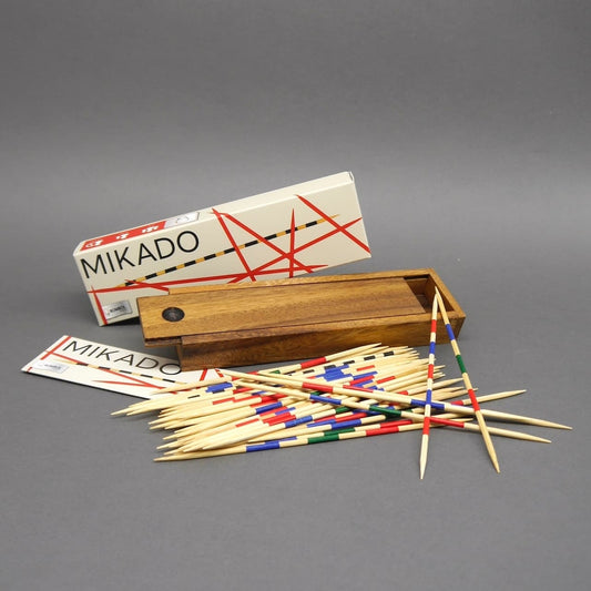 Komplettes Mikado-Set: offene Holzbox, Kartonverpackung und viele verstreute, bunt geringelte Holzstäbchen auf grauem Hintergrund.