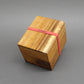 Holzwürfel-Puzzle in geschlossener Holzbox mit rotem Gummiband, ideal als Denkspiel für Knobelfreunde.