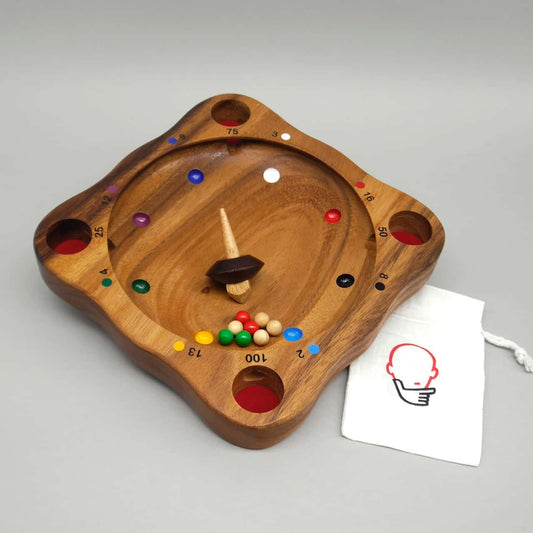 Auf dem Holzbrett „Tiroler Roulette“ rotiert ein Kreisel, bunte Kugeln sammeln sich am unteren Rand und ein Beutel liegt seitlich – spannendes Drehspiel mit Glücksfaktor.