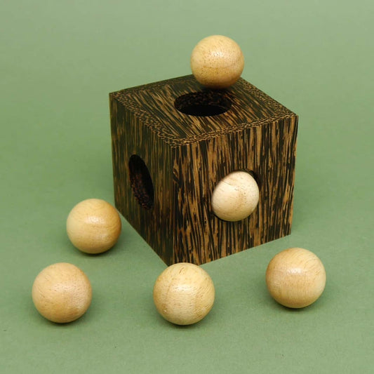 Holzwürfel mit einer Kugel obenauf und weiteren fünf Kugeln rundherum – kreatives Packpuzzle, das räumliches Denken fordert.